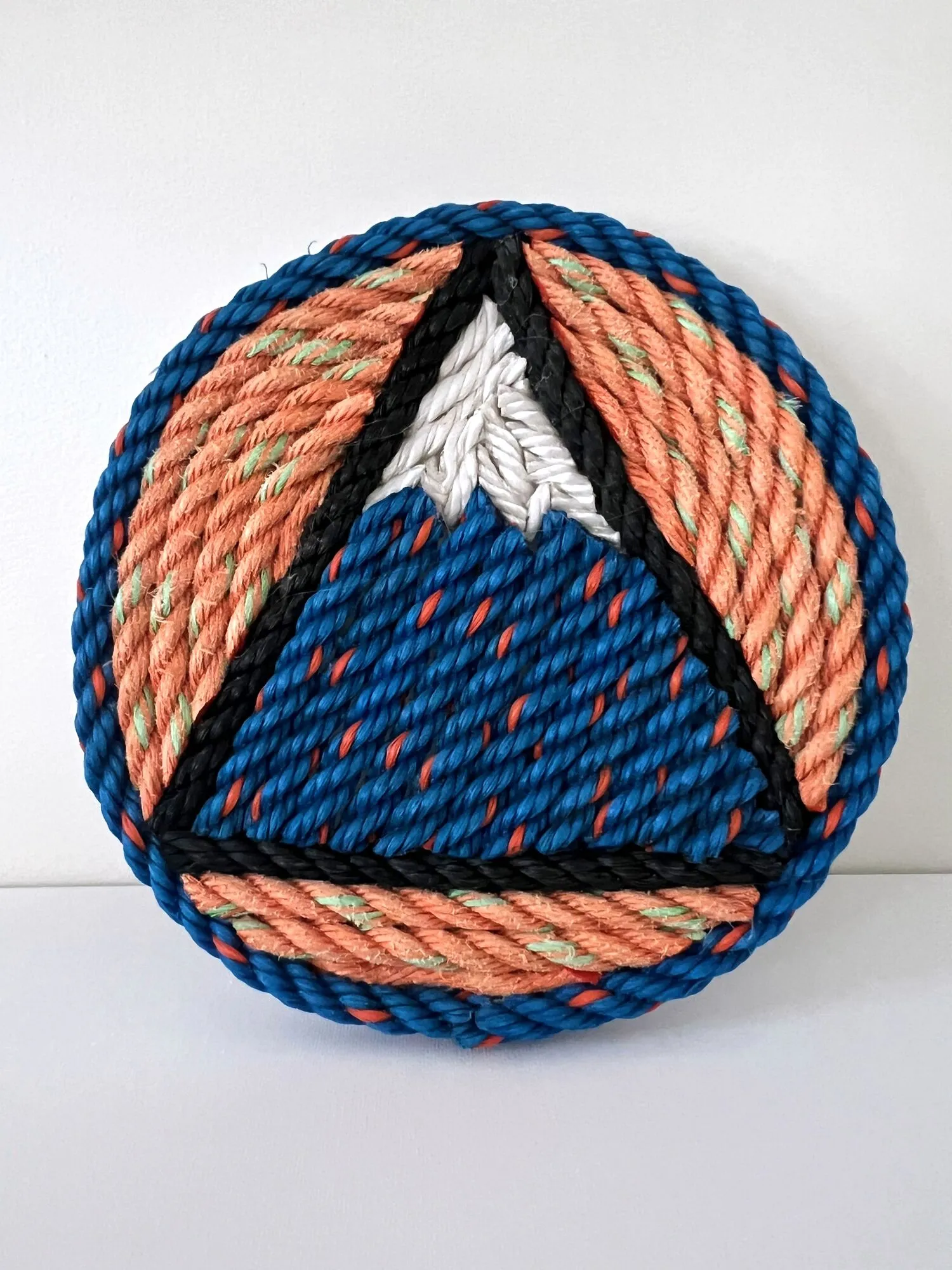 Round rope wall art of the Sugarloaf mountain logo in coral and navy